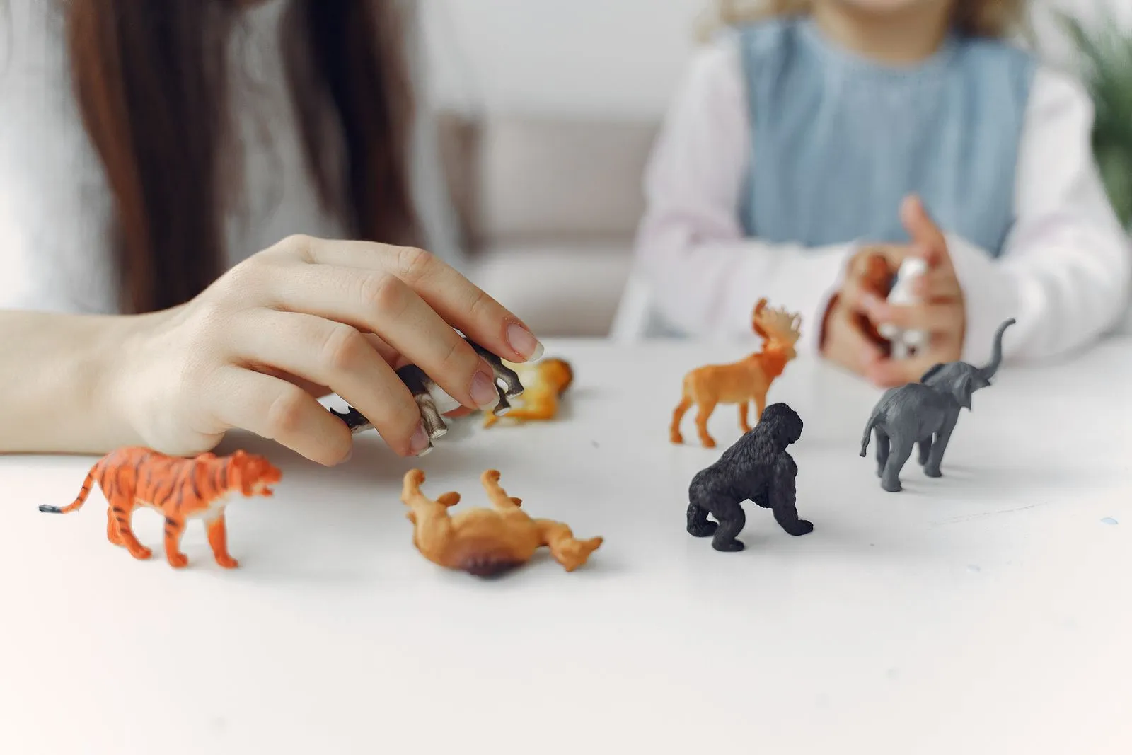 Un adult și un copil se joacă la masă cu figurine de animale.