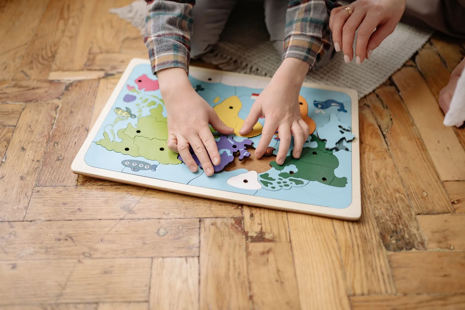 Mâinile unui copil potrivesc piesele unui puzzle din lemn, pe parchet.