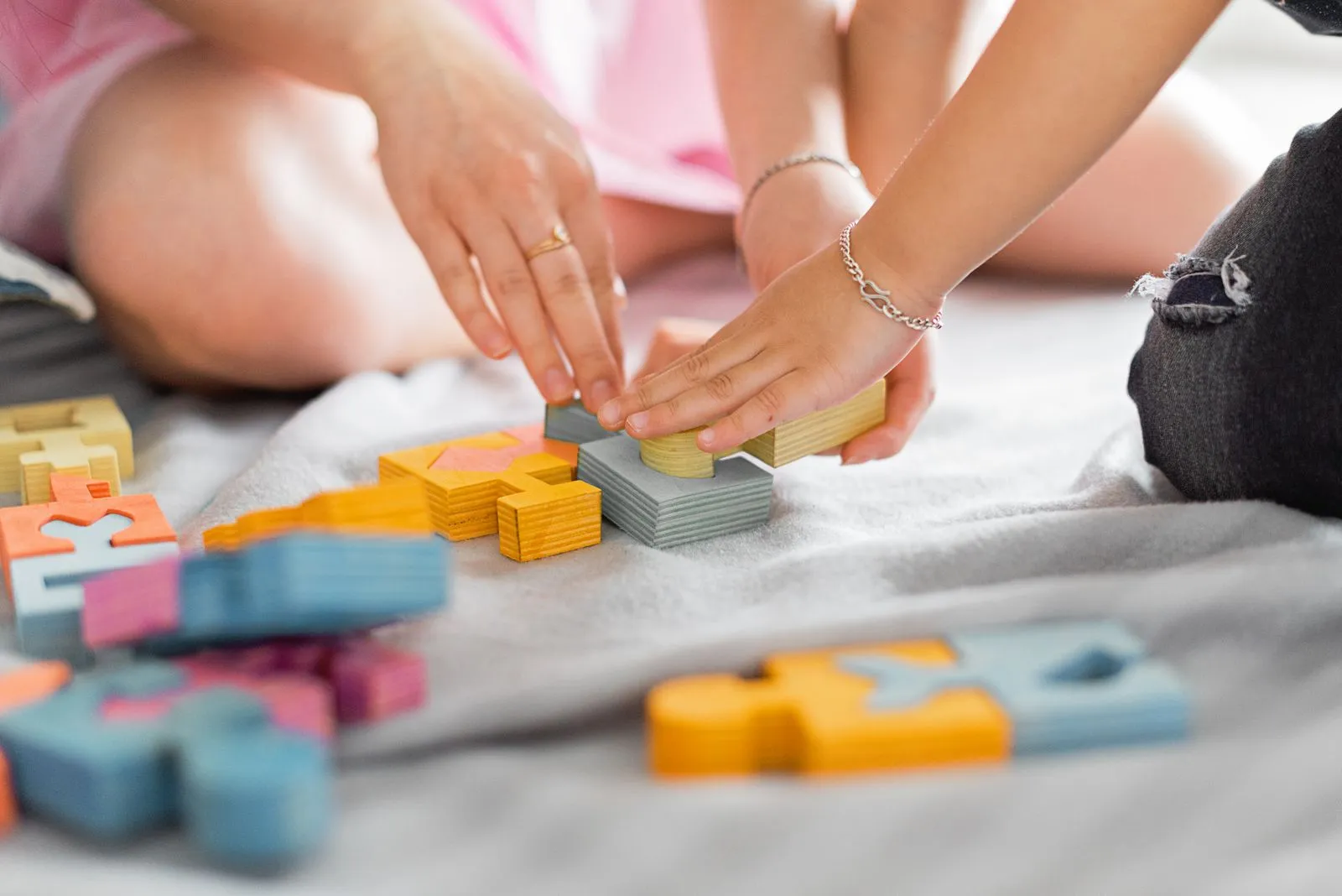 Mâinile unui adult și ale unui copil îmbină piese colorate de puzzle din lemn.